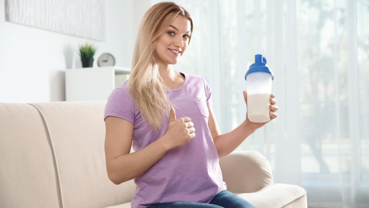 mujer joven botella batido proteinas sentada sofa casa