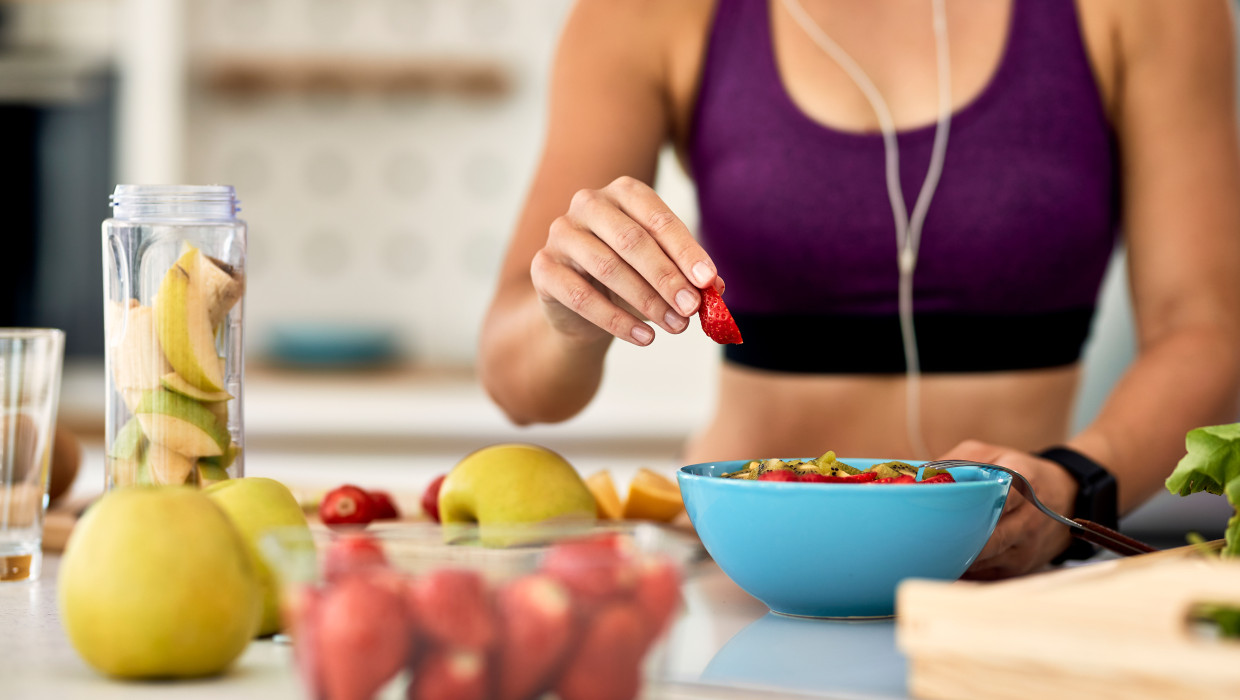 primer plano mujer atletica agregando fresas mientras hace ensalada de frutas cocina