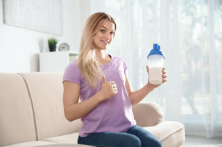 mujer joven botella batido proteinas sentada sofa casa