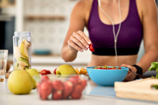 primer plano mujer atletica agregando fresas mientras hace ensalada de frutas cocina